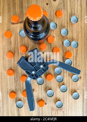 Beer brewing at home, plastic capper to put metal caps on bottles, brown glass beer bottle and orange crown caps on wooden background. Vertical image Stock Photo