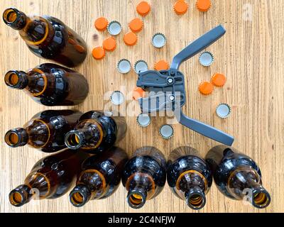 Beer brewing at home, plastic capper to put metal caps on bottles, brown glass beer bottles and orange crown caps on wooden background, horizontal ima Stock Photo