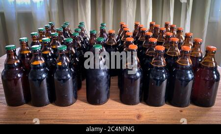 A lot of home brewery self made beer. Many brown glass craft beer bottles with green and orange corks, front view on a wooden table horizontal image. Stock Photo