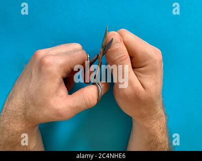 Male's hand holding on nail scissors, Man use nail scissors cutting their thumbs nail on blue background Stock Photo