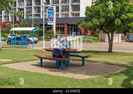Townsville, Queensland, Australia - June 2020: A couple sitting at a table in the shade having lunch near a busy coastal road Stock Photo