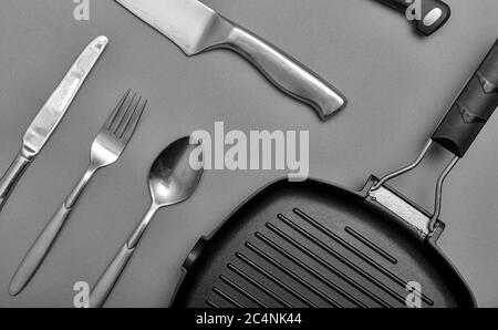 Metal knives with black on a grey table, grill pan, towel. Flat lay, layout with copy space. Stock Photo