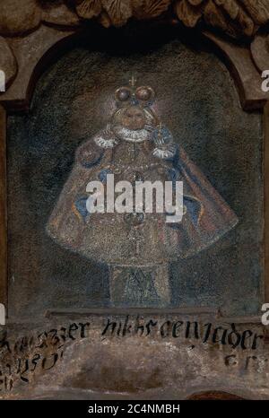 Faded painting of a 16th century wooden statue of Child Jesus, dressed in fine costume and with imperial regalia, known as the Infant of Prague.  Traditional house sign above a 1664 portal to an historic property, At The Blue Fox, now the Estonian Embassy, in Prague, Czech Republic or Czechia. Stock Photo