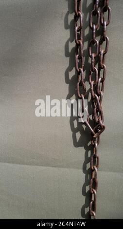 Closeup of old rusty metal chains on rough fabric background in bright sunlight with dark shadows and copy space. Broken iron chains as freedom slaver Stock Photo