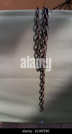 Tangled rusty metal chains hanging on rumpled tarpaulin tent. Old broken chain links as symbol of slave freedom. Industrial tools with copy space on g Stock Photo