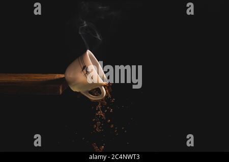 Closeup shot of a cup of hot coffee falling off the edge of a wooden table on a black background Stock Photo