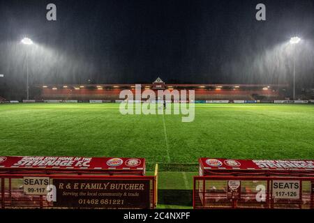 Member of grounds staff cutting grass during heavy rain at football stadium after match Stock Photo