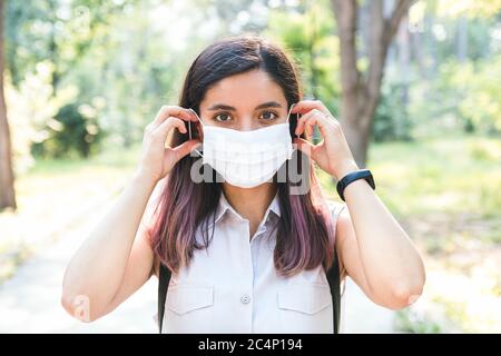 feeling free. young woman alone in park removing medical mask and breathing cheerfully Stock Photo