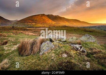 Beautiful Golden Light Shining Onto Mountains At Sunrise With Rugged Rocks In Foreground. Lake District National Park, UK. Stock Photo