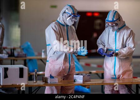 28 June 2020, North Rhine-Westphalia, Gütersloh: Helpers in protective suits disinfect their gloves after use. On the site of the former Gütersloh military airport, the German Armed Forces, together with aid organizations, have set up a smear station where people can be tested for Covid-19 after the coronary outbreak at the Tönnies meat plant. Photo: David Inderlied/dpa Stock Photo