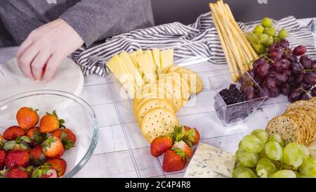 Step by step. Arranging cheese platter with fresh fruits, gourmet cheese, and crackers. Stock Photo