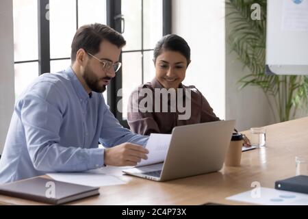 Confident businessman mentor teaching smiling Indian intern, reading documents Stock Photo