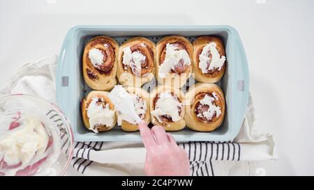 Flat lay. Glazing freshly baked cinnamon rolls in a blue baking pan. Stock Photo