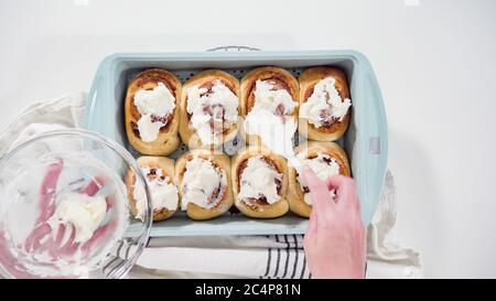 Flat lay. Glazing freshly baked cinnamon rolls in a blue baking pan. Stock Photo