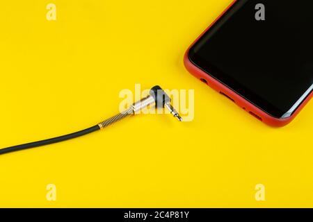 Close-up Jack plug and a cable with phone on a yellow background, top view. Stock Photo