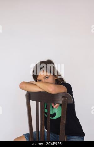 Eleven years old boy sitting on a wooden chair against a white background Stock Photo