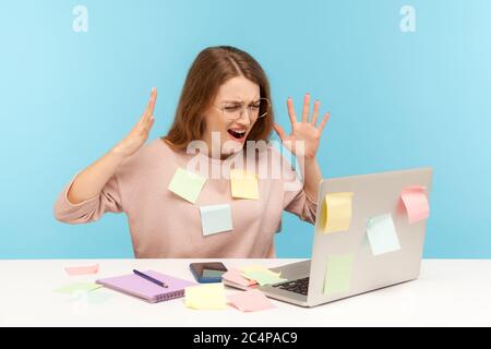 Depressed, stressed out, overworked woman employee in glasses covered with sticky notes, angrily raising hands, screaming crazy in desperate at laptop Stock Photo