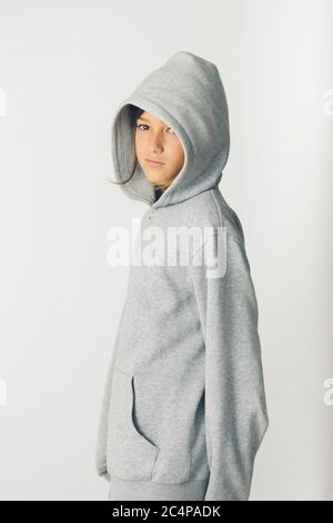 Eleven years old boy with hooded sweater standing against a white background Stock Photo