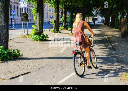 Woman rides a bicycle on a bike lane in Sweden. Girl is riding her bike on the path to Stockholm center. Stock Photo