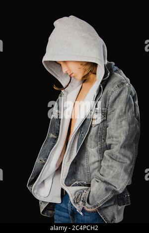 Eleven years old boy with hooded sweater and a jean jacket standing against a black background Stock Photo