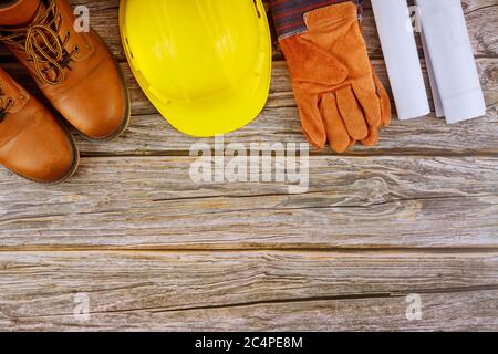 Industry worker protective workwear safety boots leather gloves yellow hard hat on architects working with blueprints in the office Stock Photo