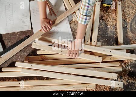 Above view of unrecognizable boy using sketches while assembling furniture in carpentry workshop Stock Photo