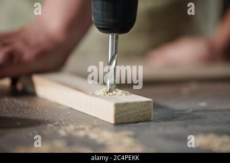 Close-up of unrecognizable carpenter drilling wooden plank to make holes at workplace Stock Photo
