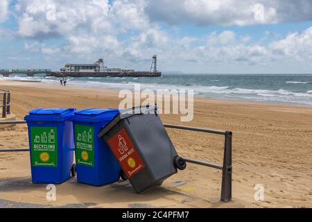 Rubbish bins, 2 recycling and one for general waste leaning over, on promenade at Bournemouth with Bournemouth beach and pier, Dorset UK in June Stock Photo