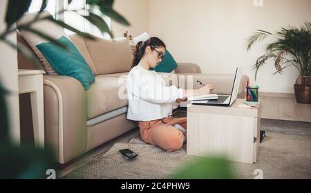 Side view photo of a concentrated caucasian woman with curly hair and eyeglasses writing something using a laptop Stock Photo