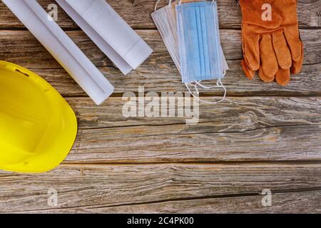 Medical wearing face medical mask for protect coronavirus covid-19 construction office engineer working blueprints house plans working yellow helmet safety protective gloves wood background. Stock Photo