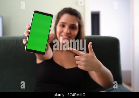 Young caucasian woman pointing at her smartphone with green screen. Chroma key. Stock Photo