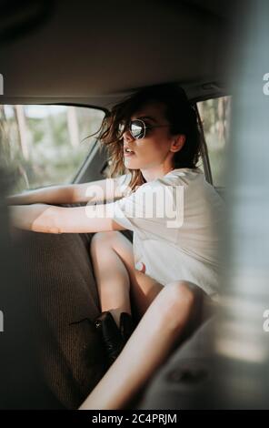 Hipster woman with sunglasses in the back seat of a car. Stock Photo