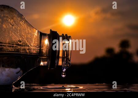 A droplet of water coming out from a bottle , reflection of the sun can be seen in the droplet. Stock Photo