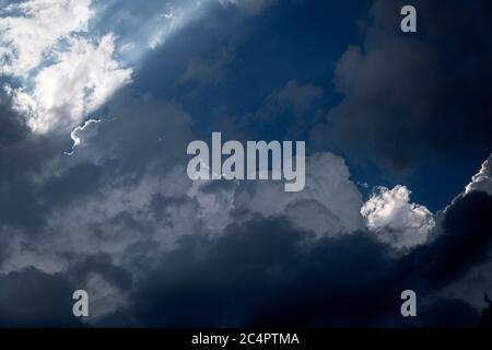 Summer Cumulus clouds backlit forming a silver lining on the edge of the formation, hiding the blue sky. 26 June 2020 Stock Photo