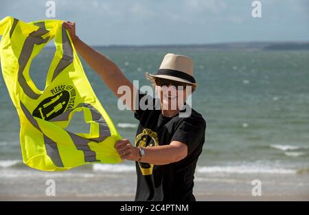 Southsea, Hampshire, England, UK. June 2020.  Woman wearing social distancing t shirt and keep your distance hi vis vest on a windy day on the beach a Stock Photo