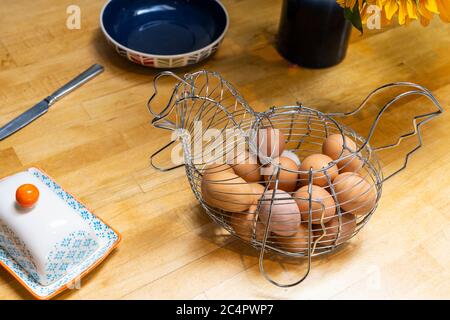 A wire basket in a chicken form holding chicken eggs on a wooden breakfast table, UK Stock Photo