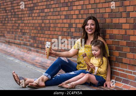 Mom and daughter eating ice cream outdoors with a brick wall in the background Stock Photo