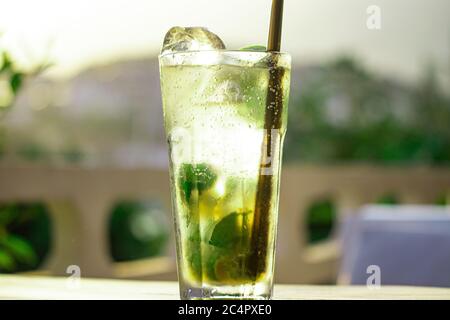 Delicious alcoholic cocktail mojito on the table with cafe landscape background. Stock Photo