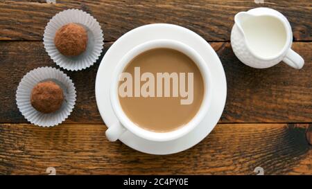 Coffee cup with cream and chocolate truffles on wooden table, top view Stock Photo