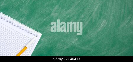 Flat lay blank squared notebook and yellow pen on green chalkboard. Top view with copy space. Back to school banner template, education concept. Stock Photo