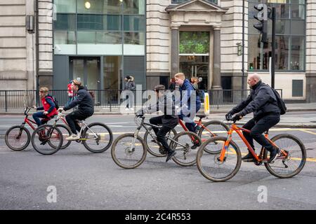 Street view of group of teenagers and one adult cycling casual careless and unprotected with no helmets on King William Street in the London City on Sunday morning, London, UK Stock Photo