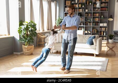 Happy father spinning little daughter, playing funny game at home Stock Photo