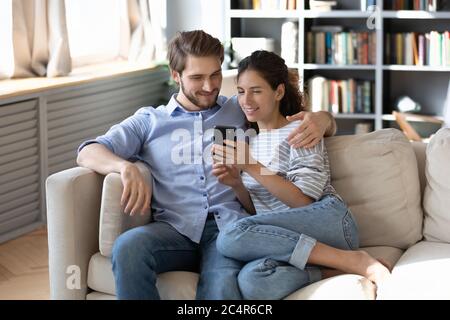 Happy young couple using smartphone together, relaxing on couch Stock Photo
