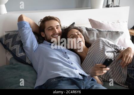 Laughing man and woman lying in bed, watching tv show Stock Photo