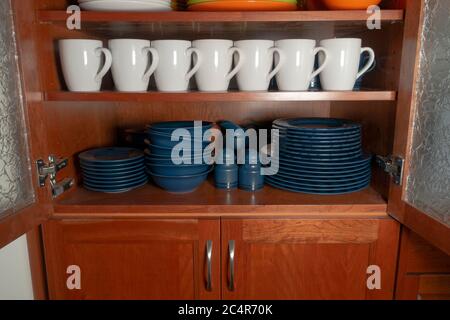 White ceramic cups and dark blue crockery are neatly organized in a cupboard. Good housekeeping concept Stock Photo
