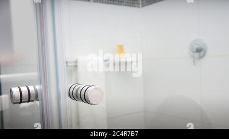 Bath with glass doors and walls of white ceramic with towel and shampoo inside Stock Photo