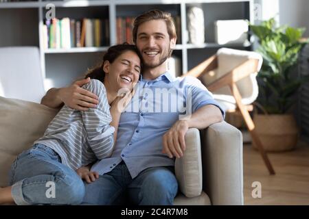 Happy young couple hugging, laughing at joke, sitting on couch Stock Photo