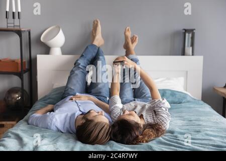Happy young couple relaxing on bed together, using smartphone Stock Photo