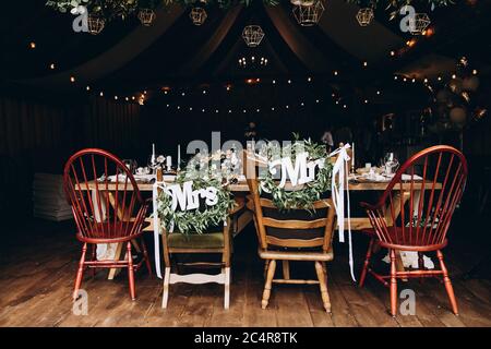 Dark wooden chairs decorated with white letters "Mrs" and "Mr" standing around festive table. Concept of wedding details and stylish decoration. Stock Photo