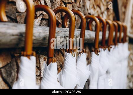 White wedding umbrellas hanging in row on wooden wall. Beautiful decoration for stylish event. Protection for guests from rain or sun. Stock Photo